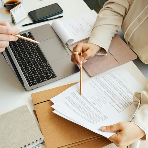 pexels-photo-7876786-7876786 Top view of colleagues working together with a laptop and documents in an office setting.